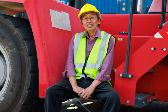Look at camera sitting on crane. Portrait elder asian dock worker working at Cargo container yard. Marine and carrier insurance concept. cargo shipping container box in logistic shipping yard