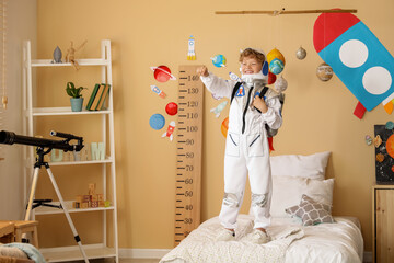 Happy young boy in astronaut costume standing on bed with space-themed room decor and telescope © Pixel-Shot