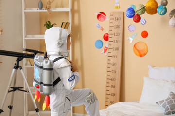 Young boy in astronaut costume with DIY jetpack standing in space-themed bedroom with growth chart and telescope, the room features a wooden growth chart with space decals, hanging planet models © Pixel-Shot