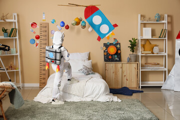 Child in astronaut costume playing in space-themed bedroom with rocket decor and solar system mobile © Pixel-Shot