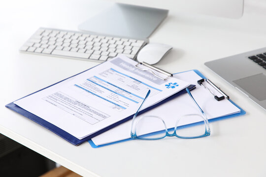 Health insurance form with eyeglasses and laptop on white desk, medical coverage and healthcare planning, the arrangement suggests a professional environment for managing health-related documents