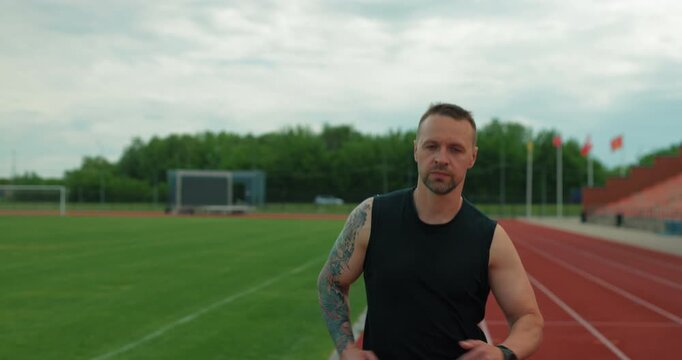 Focused male runner with sleeve tattoo training on a sports field background
