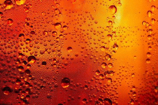 A close-up image of condensed water droplets on a cold glass surface against a warm golden background; Kola Macro beverage texture,A macro photograph capturing intricate water droplets.