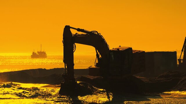 Excavator silhouette digging sand at sunset