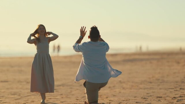 Couple plays catch on the beach during sunset in California while others walk in the background