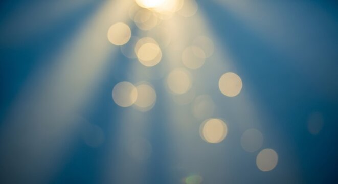 Abstract blue background with soft golden bokeh circles and light rays shining from above frame
