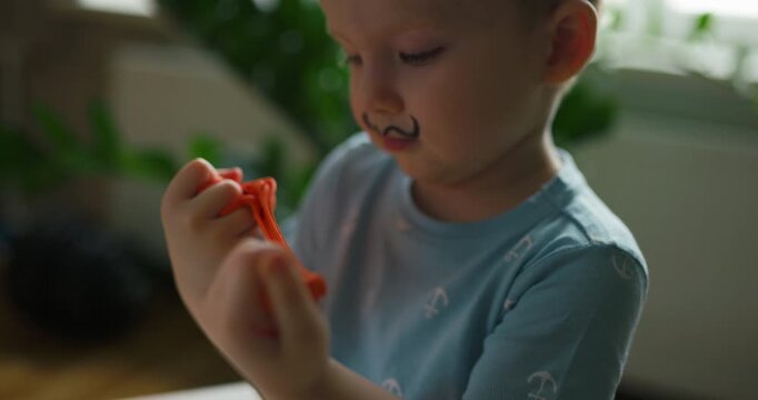 Funny little boy with painted mustache playing with orange modeling clay