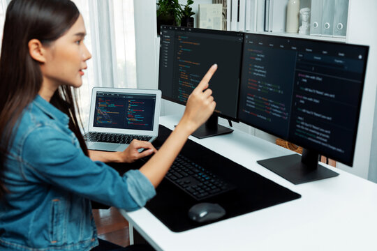 Young Asian girl of IT developer pointing online information on pc with coding program data application on website project, wearing jeans shirt. surrounded by safety programing two screens. Stratagem.