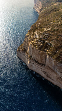 high angle drone view looking down at dingli cliffs chalky limestone coast on south malta island coast with Mediterranean Sea below at summer sunset golden haze above with green foliage on the land