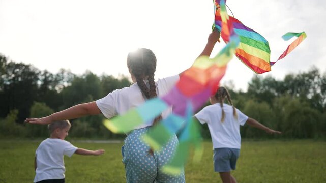 Children flying kite at sunset. Kids run in park with colorful kite. Happy children enjoy summer evening. Sunset fun in park with kite. Group Children flying kite. Children playing outdoors at sunset.