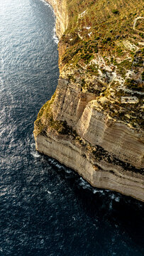 high angle drone view looking down at dingli cliffs chalky limestone coast on south malta island coast with Mediterranean Sea below at summer sunset golden haze above with green foliage on the land