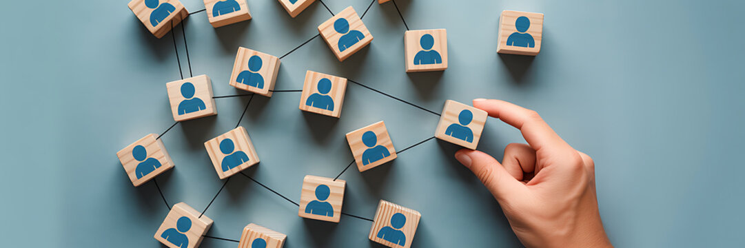 A hand placing a wooden block with a human icon into a network of connected blocks on a blue background