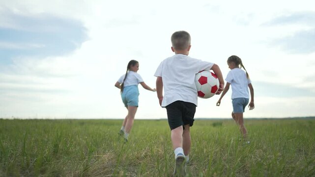 Children play with ball. Group Children enjoy outdoor activity together. Happy children run with soccer ball in meadow. Active lifestyle concept for children. Kids group having fun with ball teamwork.