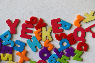 Fototapeta premium Vibrant and colorful plastic magnetic alphabet letters piled together in a chaotic design layout on a solid white tabletop background