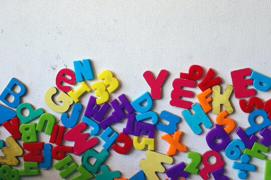 A jumbled pile of vibrant multi colored plastic toy alphabet magnets scattered randomly on a clean white horizontal surface backdrop