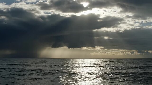 Dramatic storm clouds break to reveal golden sunlight over the ocean waves.