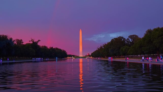 Sunset rainbow over Washington Monument and Reflecting Pool, Washington, D.C. Vivid pink and purple sky with obelisk reflection on rippled water surface.