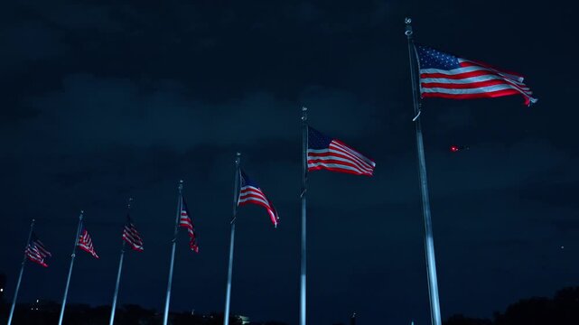Row of American flags on flagpoles against dark night sky, Washington DC. Low angle view of flags waving in wind with cloudy overcast backdrop.