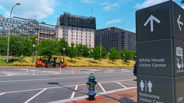 White House visitor center directional sign, Washington D.C. Street view with hydrant, scaffolding, and government buildings under clear summer sky.
