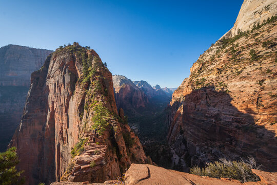 Hikers navigating the steep narrow ridge of the Angels Landing trail in Zion National Park with a deep canyon below.