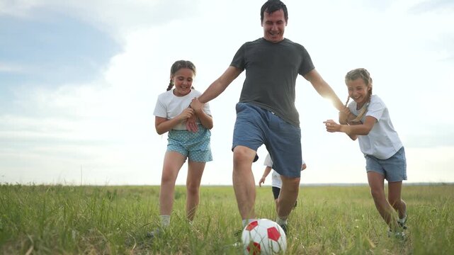 Happy family playing ball together in park. Father and children enjoying a sunny day, chasing ball on green grass. children laughing and smiling while father guides. Summer outdoor fun for family.