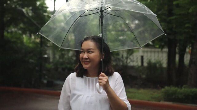 Asian middle-aged woman using umbrella after light raining, preparing for rain season, rainfall in rainy monsoon season