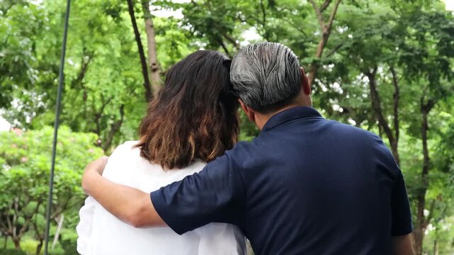 Happy Asian senior couple, elderly husband and wife hugging each other in urban park with good quality of life togetherness after retirement, real human, back view
