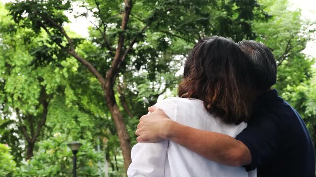 Happy Asian senior couple, elderly husband and wife hugging each other in urban park with good quality of life togetherness after retirement, real human, back quarter view