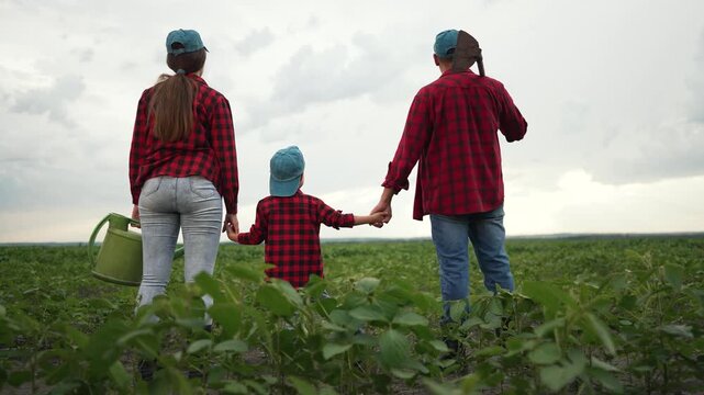 Family farmers with child in field hoe and sprinkler . Family holding hands in field with hoe and sprinkler. Happy family farming lifestyle. Parents and child in matching outfits. Rural life concept.