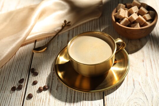 Aromatic coffee in cup, brown sugar, beans and spoon on wooden table, closeup