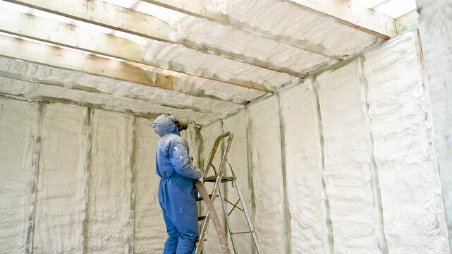 Technician applies polyurethane foam insulation to unfinished timber wall. Expanding coating forms airtight coverage for renovation, construction, and energy saving
