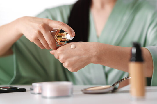 Woman applying foundation onto her hand at table indoors, closeup