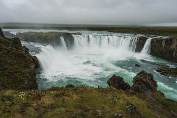 Obraz premium Wide view of the spectacular Godafoss waterfall in Iceland with turquoise water cascading over rocky cliffs.