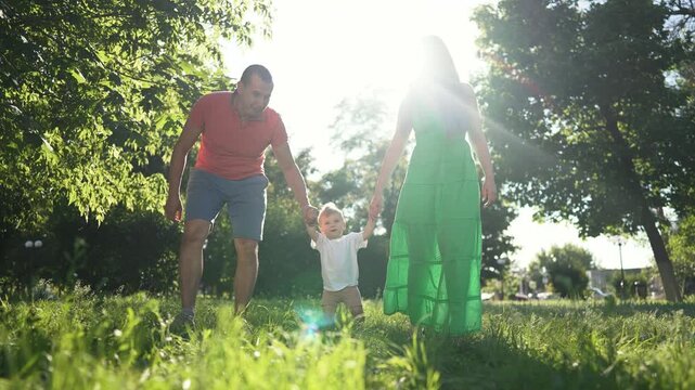 Child taking first step with family. Mom and father guide child in park. First moments walking with parents support. family bonding as child takes first step. Child learning to walk with family help.