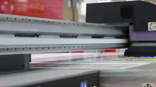 Large format uv printer printing colorful image on flat surface in motion, close up view of printing head moving and lights.