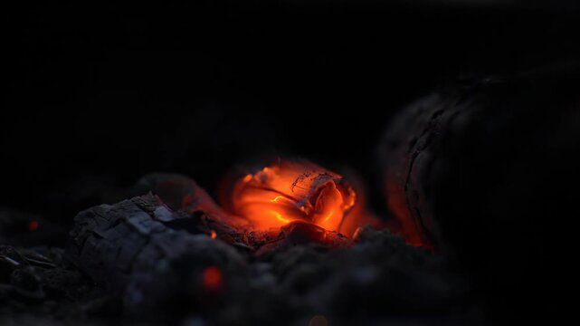 Hot glowing embers smoldering in burnt wood at night while small sparks rise and Bokeh lights glow warm