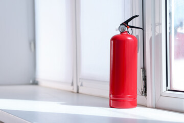 Fototapeta premium One red fire extinguisher near window indoors, space for text