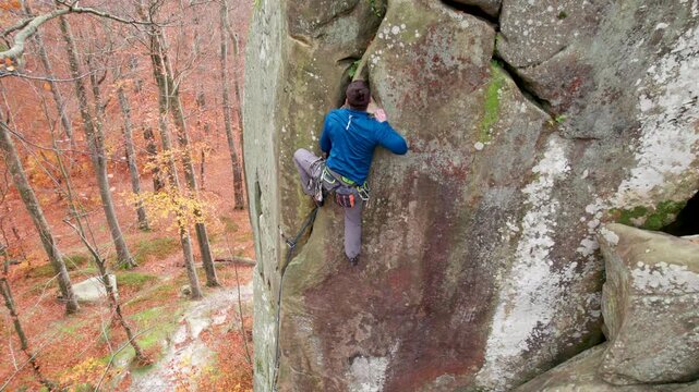 Drone shot of athlete tackling natural rock route high above woodland floor. Cinematic climbing footage for performance, courage, resilience, and outdoor recreation branding