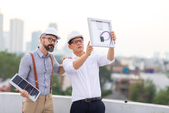 Hipster business man and Office building owner and energy engineer in hardhat helmet plan a project to build a solar panel for the building under construction.