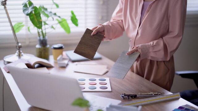 Interior designer comparing wood and material samples while reviewing furniture design color palette and textures on bright minimalist desk in modern studio