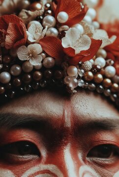 Primo piano di un volto con trucco tribale rosso e ricco copricapo di perle e fiori (Generato dall'IA)