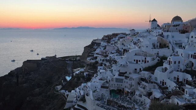 Whitewashed houses cascade down cliffs above the Aegean Sea at dusk in Oia, Santorini, Greece, with pastel sunset sky and calm water.