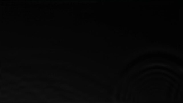 Clean water ripples and circular liquid rings expanding outwards against a pitch black background.