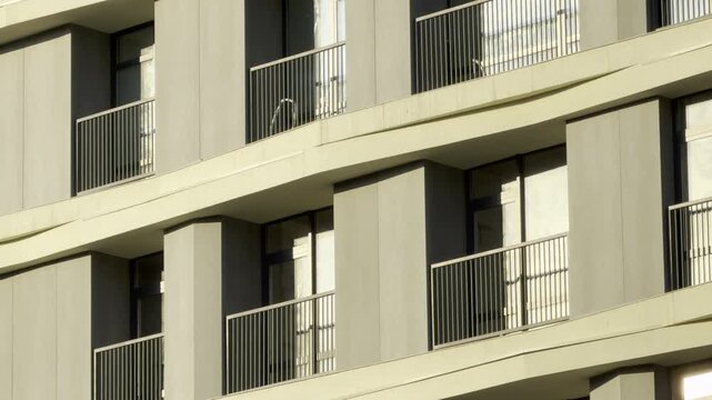 Modern minimalist balconies stretch across a clean concrete building facade. The elegant geometric design creates a calm and secure feeling for city residents.