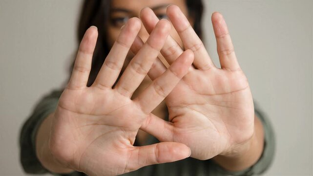 Young woman holding hands up in a defensive stop gesture with blurred face, symbolizing rejection, boundaries, and protection against harassment or violence.