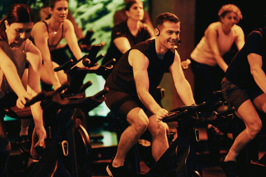 Indoor cycling class with smiling instructor leading a diverse group workout at a boutique gym