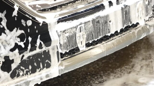 The car with soap sponge washing process, active foam flows off the car body. Second phase of detailing washing in car service. Cleaning the car using high pressure water. Process of spraying foam. 