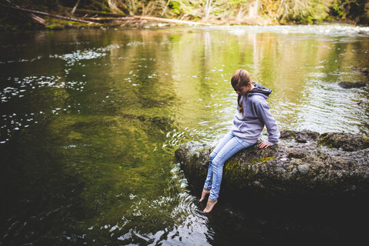 A girl sitting on the edge of a rock over a creek