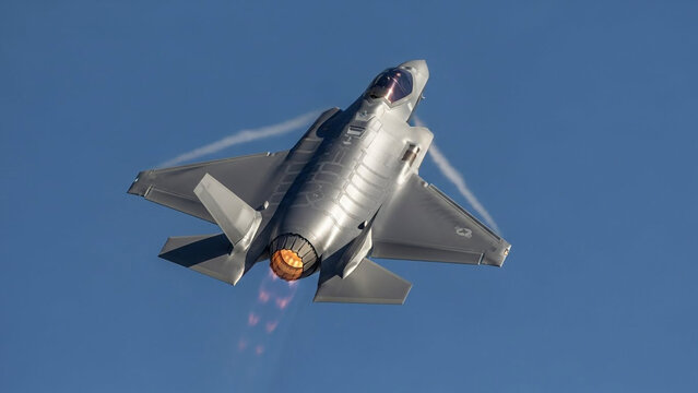 F-35 Lightning II Stealth Fighter Jet in High Speed Flight with Afterburner Engaged and Vapor Trails in Blue Sky