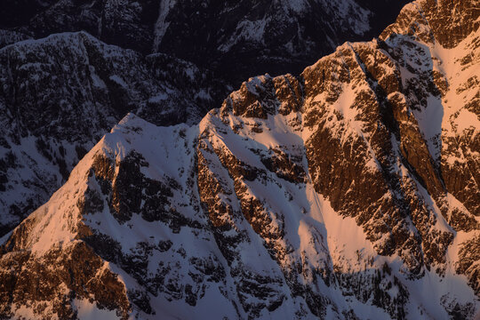 Snowy mountain peaks lit by sunset glow from a distant horizon
